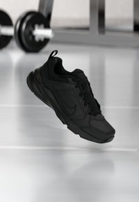 Sort sportsko med en glat syntetisk overdel, snørebånddesign, polstret krave og struktureret sål. Har diskret branding.