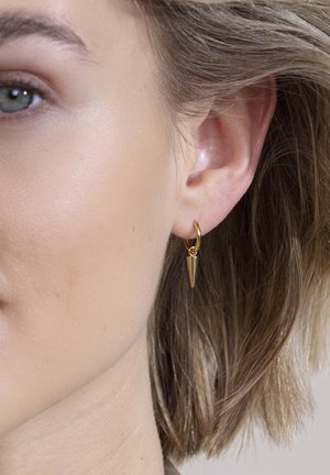 Goldene Creolen mit einem dekorativen, spitzen Pendel in Form eines Kegels. Glatte Textur mit glänzender Oberfläche, designt für Ohrlöcher.