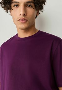Paarse katoenen T-shirt met een ronde halslijn en korte mouwen. Glad van structuur zonder zichtbare patronen of hardwaredetails.