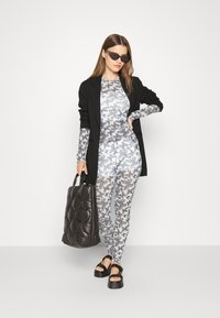 Leggings estampados com impressão de borboletas em monocromático, combinados com um blazer preto ajustado, sandálias pretas robustas e uma bolsa tote preta acolchoada.