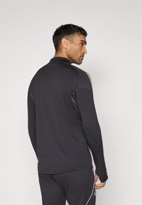 Black long-sleeve athletic top with high collar, featuring side panels, yellow and pink accents, and a sleek, smooth texture.
