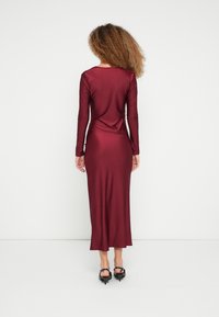 Bordové šaty s dlhým rukávom a priliehavým strihom, s hladkou textúrou a dizajnom po zem, s jemným záhybom na chrbte.