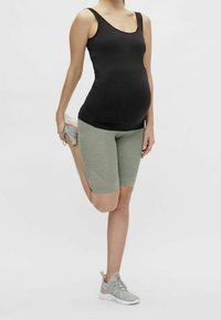 Svart, ärmlös tanktopp i kombination med ljusgröna, strukturerade shorts i knälängd. Modellen utför en bensträckning medan hon håller en sneakers.