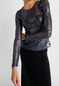 Černý top s dlouhými rukávy vyrobený z průsvitné síťoviny, zdobený stříbrnými flitrovými diamantovými vzory a kulatým výstřihem, doplněný černou sukní.