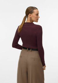 Maglia a maniche lunghe ribbed bordeaux con colletto, abbinata a pantaloni beige a vita alta con tasche posteriori e una cintura nera.