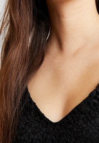 Svart spetsplagg med V-ringning, prytt med blommönster och en delikat textur som kompletterar den släta hudtonen underneath.