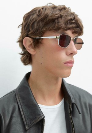 Metalliske rektangulære solbriller med mørke linser, tynd sølvramme og subtile guldaccentuer, parret med en sort læderjakke og hvid skjorte.