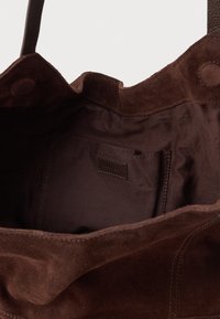 Barna velúr bevásárlótáska puha, jellegzetes felülettel, tágas belső résszel és egy kis belső zsebbel, amelyen címke található.