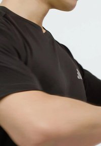 Černé sportovní tričko s výstřihem do V, krátkým rukávem a decentním logem na hrudi. Má hladkou, lehkou tkaninu.