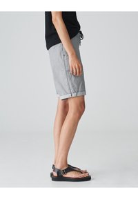 Gray striped shorts with rolled hems, made from lightweight fabric. Paired with black flat sandals featuring a buckle strap.