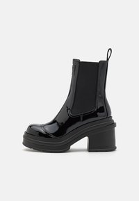 Botas negras de tobillo con un acabado brillante de charol, paneles laterales elásticos, una plataforma gruesa y un tacón cuadrado ancho para mayor estabilidad.