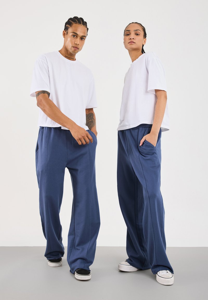 T-shirt bianco a maniche corte abbinato a pantaloni della tuta blu navy larghi con tasche laterali. Tessuto testurizzato, design casual.