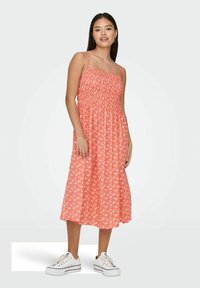 Koralo midi suknelė su baltais gėlių raštais, surinkta liemeni, plonomis petnešėlėmis ir plazdančiu sijonu. Suderinta su baltais sportbačiais.