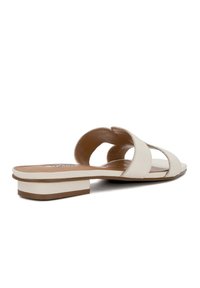 Beige leren slippers met open ontwerp, voorzien van gekruiste bandjes en een kleine blokhak. Glad oppervlak en minimalistische stijl.