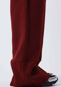 Bordeauxrode joggingbroek gemaakt van zachte stof, met een losse pasvorm en rechte pijpen, gecombineerd met zilveren en zwarte sportschoenen.