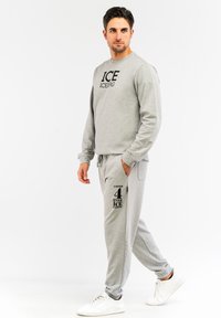 Sivi dukserica s logotipom "ICE", u paru sa sivim trenerkama koje imaju džep i crni print. Bijele tenisice upotpunjuju outfit.
