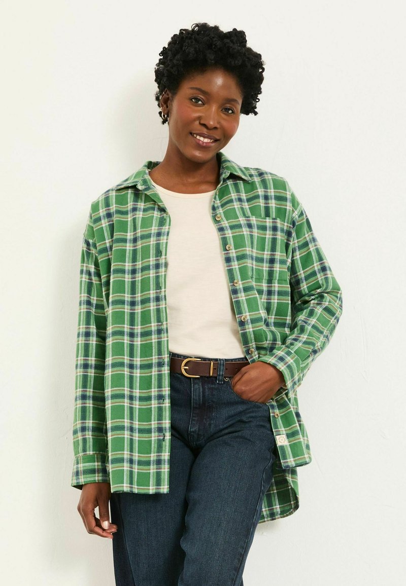 Green plaid shirt with white and navy accents, button-down front, long sleeves, worn over a light-colored top and dark jeans.