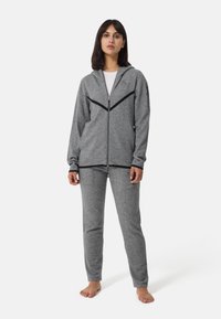 Grå zip-up hoodie med svarta accenter och logotyp, i kombination med grå byxor. Mjuk, texturerad tyg, figurnära design och minimalistisk stil.