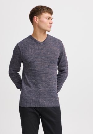 Suéter de punto en V color azul oscuro con un patrón texturizado, que presenta mangas largas y un dobladillo acanalado, combinado con pantalones negros.