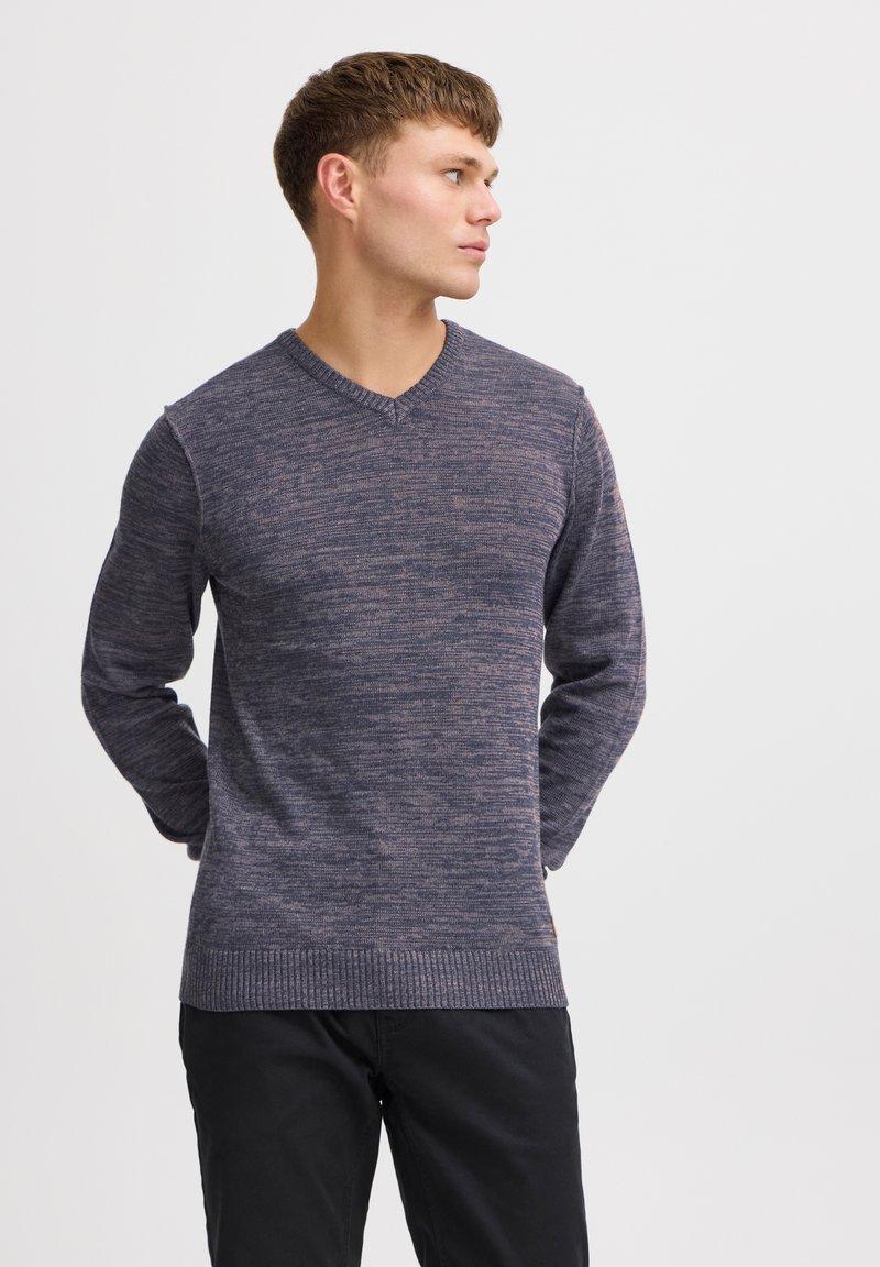 Maglione a V in maglia di colore blu scuro con un motivo testurizzato, dotato di maniche lunghe e orlo a costine, abbinato a pantaloni neri.