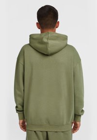 Olivengr�øn hoodie med en stor hætte, brede ærmer og ribbede manchetter. Lavet af blødt stof med en let tekstureret overflade.