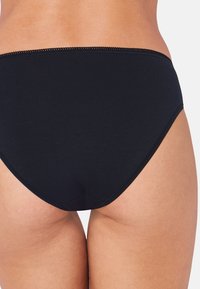 Schwarze Baumwoll-Hipster-Unterwäsche mit glatter Textur, die einen dezenten gewellten Rand entlang des Bundes und ein vollständig bedeckendes Rückendesign aufweist.