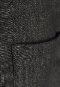 Tmavě šedá látka s texturovanou vazbou. Obsahuje viditelnou kapsu na jedné straně, což zvýrazňuje švy podél okrajů.