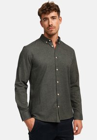 Chemise boutonnée vert foncé avec une finition texturée, col pointu et boutons marron. Caractéristiques : manches longues et ourlet droit.