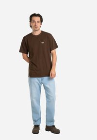 Camiseta de algodón marrón con cuello redondo y mangas cortas, combinada con jeans de mezclilla azul claro y botas marrones con cordones.