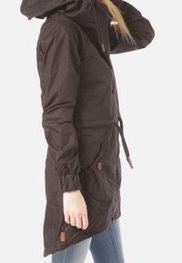 Svart parka med huva, med ett prickigt mönster. Elastiska ärmslut, dragsko i midjan och knäppbara fickor ger funktionalitet.