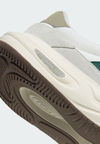 Gros plan de la semelle d'une basket gris clair et blanche avec une bande de roulement marron et le logo visible "Cloudfoam" sur la semelle intermédiaire latérale.