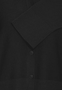 Fekete kötött kardigán. Bordázott mandzsettával és szegéllyel, elöl négy gombbal záródik. Egyszerű, díszítés nélküli kialakítás.