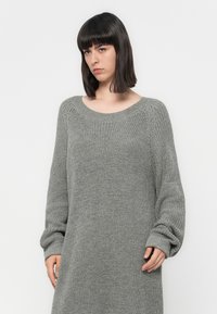 Sivkasta pletenega puloverja z širokim izrezom in dolgimi, rahlo nabranimi rokavi. Ima teksturirano blago in ohlapen, sproščen kroj.