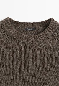 Pull marron en maille épaisse avec col rond côtelé et étiquette indiquant "Massimo Dutti, Fabriqué en Espagne."