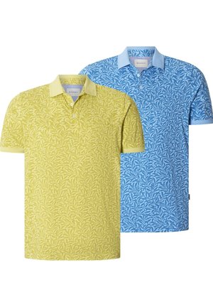 Mann trägt gelbes kurzärmeliges Poloshirt mit Blattmuster und dunkelblaue Hose, steht mit einer Hand in der Tasche vor weißem Hintergrund.