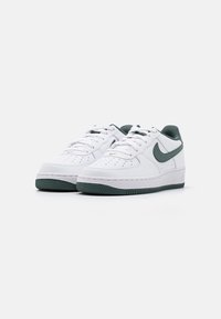 Białe skórzane sneakersy z zielonymi akcentami, okrągły czubek, perforowane detale na nosku, płaskie sznurówki i teksturowana gumowa podeszwa.
