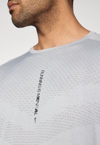 Αθλητικό πουκάμισο ανοιχτού γκρι χρώματος με στρογγυλή λαιμόκοψη, με υφή από δίχτυ και μαύρο κείμενο που γράφει "ΤΟ ΤΡΕΞΙΜΟ ΕΙΝΑΙ ΨΥΧΙΚΟ" με το λογότυπο της Nike.