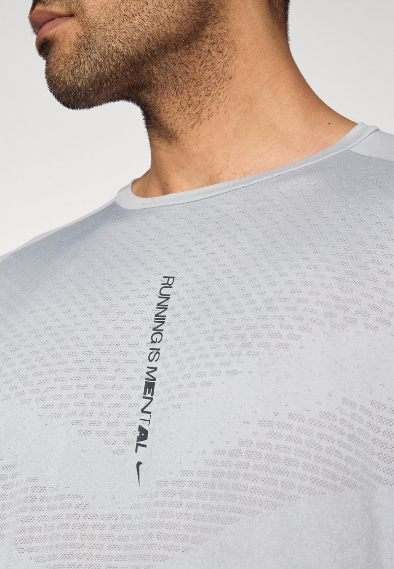 Maglietta sportiva grigio chiaro con scollo rotondo, caratterizzata da una trama a rete e testo nero con la scritta "RUNNING IS MENTAL" accompagnata dal logo Nike.
