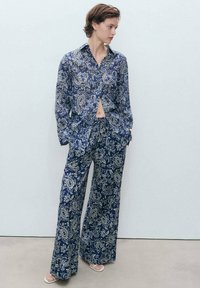 Set di camicia a righe navy e pantaloni a gamba larga con design floreali e paisley. Il tessuto sembra leggero e liscio.
