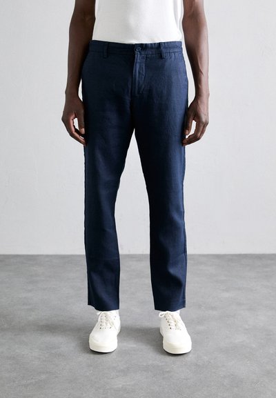 Marineblauwe linnen broek met een rechte pasvorm, voorzien van een knoopsluiting, riemlussen en zijzakken. Gepaard met witte sneakers.