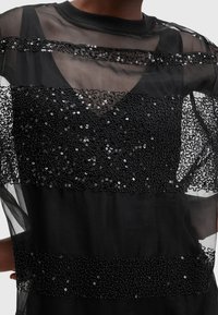 Haut noir transparent avec des bandes horizontales de sequins noirs, sur une base en tissu noir uni et un col rond. Texturé et léger.