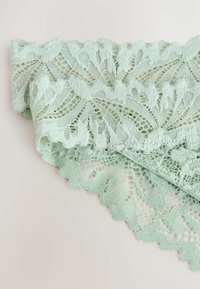 Tissu en dentelle vert menthe avec des motifs de feuilles complexes et des bords festonnés. La texture transparente avec des densités de fil variées ajoute un intérêt visuel.