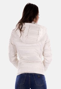Giacca a vento bianca imbottita con cuciture orizzontali, cappuccio e polsini elasticizzati, abbinata a jeans blu. Design testurizzato e imbottito per garantire calore.