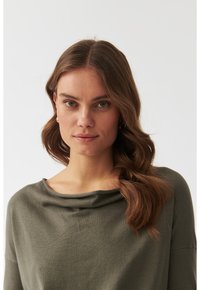 Top olive verde cu decolteu drapat și mâneci trei sferturi, fabricat dintr-un material moale. Textură netedă, croială confortabilă.