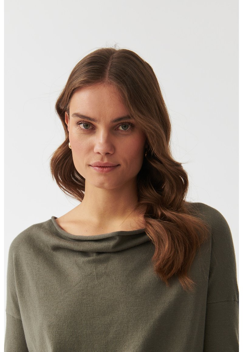 Top verde oliva con scollatura drappeggiata e maniche a tre quarti, realizzato in tessuto morbido. Texture liscia, fit rilassato.