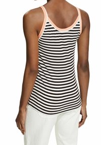 Top de tirantes a rayas en blanco y negro con acentos en rosa. Presenta un diseño de espalda nadadora y tejido suave. Usado con pantalones blancos.