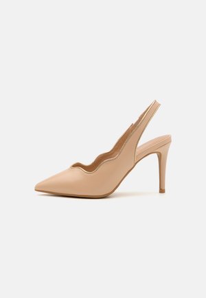 Beżowy szpiczasty but na obcasie typu slingback z falistymi krawędziami i szpilkowym obcasem na białym tle.