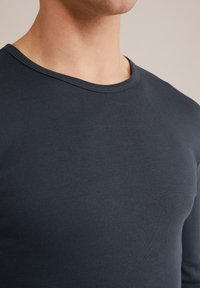 Artimas kadras, kuriame matoma tamsiai mėlyna visas kaklo apvalkalo marškinėliai, rodančius iškirptę, viršutinę krūtinės dalį ir dalį kaklo bei žandikaulio.