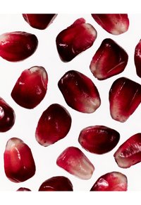 Graines de grenade de formes variées, présentant une surface brillante de couleur rouge profond avec des bords translucides sur un fond blanc.