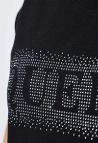 Tela negra con brillantes rhinestones dispuestos de manera densa para formar un patrón rectangular estilizado con formas redondeadas en su interior.